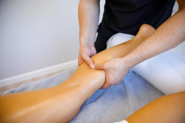 Male sports massage therapist treating calves of a a woman patient